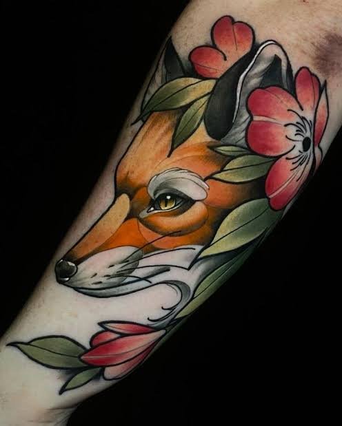 Tatuaje neotradicional de zorro rodeado de flores y hojas ornamentales.